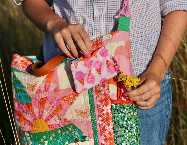 Op de afbeelding: Een kleurrijke patchwork tote bag met een bijpassend klein etui met ritssluiting. De tas heeft verschillende patronen, waaronder vlinders, bloemen en geometrische vormen in roze, oranje, groen en geel. Het kleine etui heeft een roze ijsjespatroon.