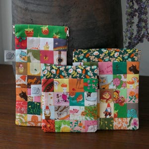 May include: Three rectangular fabric pouches with metal squeeze frames, featuring a patchwork design of colourful squares with various illustrations including gnomes, animals, flowers, and food, and a small white tag with a snail icon on the side.