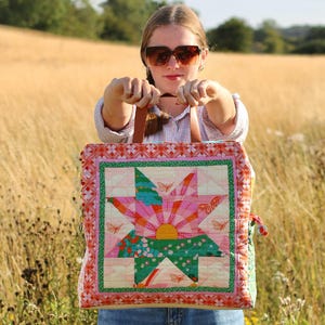 Op de afbeelding: Een kleurrijke gewatteerde tote bag met een sterrenpatroon in roze, groen en oranje tinten. De tas heeft een vierkante vorm, een leren handvat en een decoratieve rand. Vlinders zijn verspreid over het ontwerp.