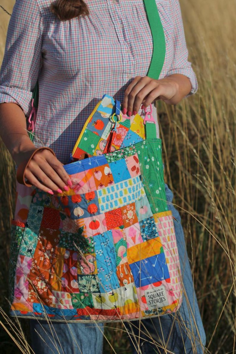 Op de afbeelding: Een patchwork tote bag met een groene band en een bijpassend etui met ritssluiting. De tas heeft een verscheidenheid aan kleurrijke stoffen vierkanten met fruit-, bloemen- en geometrische patronen. De tekst "SQUARE STORIES" is zichtbaar.