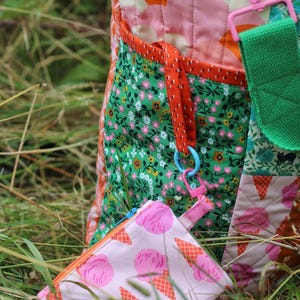 Op de afbeelding: Een kleurrijke gewatteerde tote bag met een bijpassend klein etui met ritssluiting. De tas heeft bloemen- en abstracte patronen in roze, oranje en groen. Het etui heeft een roze ijsje-ontwerp.