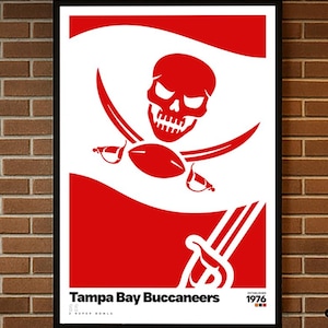 Puede incluir: Un póster enmarcado con el logotipo de los Tampa Bay Buccaneers. El diseño incluye una calavera roja y espadas cruzadas sobre un fondo blanco, con el nombre del equipo y el año 1976 en la parte inferior. El póster está colgado en una pared de ladrillo.