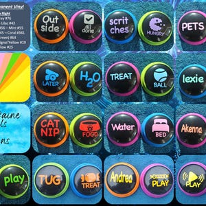 Puede incluir: Un conjunto de 20 botones redondos y coloridos con diferentes palabras e imágenes impresas en ellos. Los botones están diseñados para ser utilizados con un sistema de entrenamiento para perros. Las palabras en los botones incluyen "jugar", "golosina", "comida", "agua", "cama", "pasear", "afuera", "amigo", "hambriento", "querer", "pelota", "hierba gatera", "más tarde", "rompecabezas", "tirar", "lexie", "akenna", "andrea", "scriches", "mascotas".