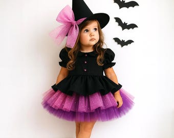 May include: A child's Halloween witch costume. The outfit includes a black dress with a layered purple and pink tulle skirt, a black witch hat with a pink bow, and black boots. Decorative black bat cutouts are on the wall.