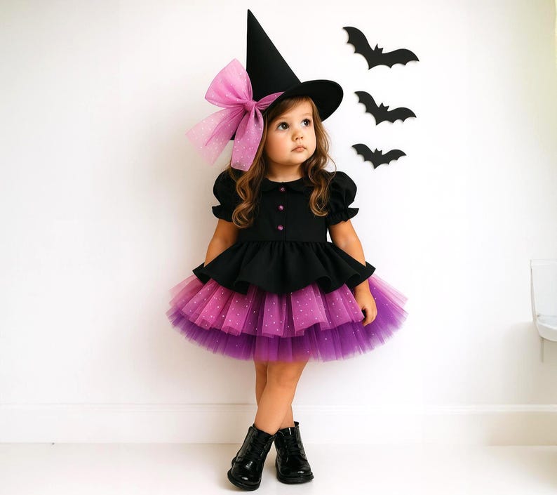 May include: A child's Halloween witch costume. The outfit includes a black dress with a layered purple and pink tulle skirt, a black witch hat with a pink bow, and black boots. Decorative black bat cutouts are on the wall.
