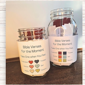 Peut inclure: Deux bocaux en verre avec des étiquettes blanches qui indiquent "Versets bibliques pour le moment" et "Prenez-en un lorsque vous vous sentez..." avec des sections codées par couleur pour différentes émotions. Les bocaux sont remplis de petits morceaux de papier.