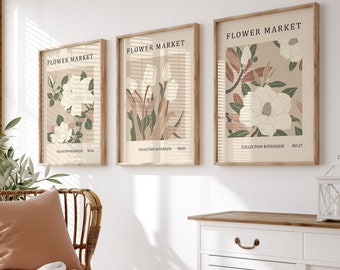 May include: Three framed botanical prints with the title "Flower Market" and the text "Collection Botanique" in a light brown frame on a white wall. The prints feature illustrations of white flowers with green leaves on a beige background.