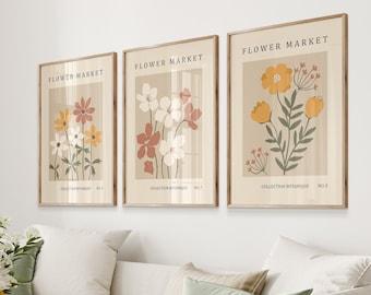 May include: Three framed prints with a beige background and floral illustrations. The prints are titled "Flower Market" and feature different floral arrangements in shades of yellow, orange, red, and white. The text "Collection Botanique" and a number are printed below each illustration.