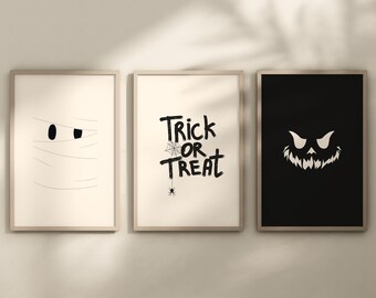 May include: Three framed Halloween-themed prints. The left print features a white mummy with black eyes. The middle print has black text that says "Trick or Treat" with a spider and web. The right print is black with a white silhouette of a jack-o-lantern.