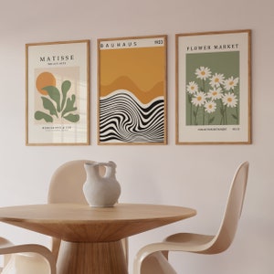 May include: Three framed art prints with minimalist designs. The left print features a green plant with a yellow sun, the middle print has a black and white wavy design with a yellow background, and the right print has white daisies on a green background.