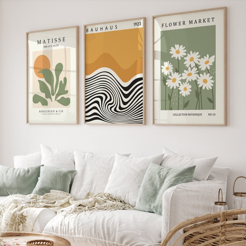 May include: Three framed art prints with a minimalist design. The left print features a green plant with a yellow sun, the middle print has black and white wavy lines on a yellow background, and the right print has white daisies on a green background. The prints have the text "Matisse", "Bauhaus 1923", and "Flower Market" respectively.