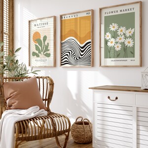 May include: Three framed art prints with a minimalist design. The left print features a green plant with a yellow sun in the background. The middle print features black and white abstract lines. The right print features white daisies on a green background. The prints are labeled "Matisse", "Bauhaus 1923", and "Flower Market".