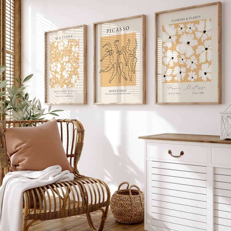 K&ouml;nnte beinhalten: Drei gerahmte Kunstdrucke mit minimalistischer &Auml;sthetik. Die Drucke zeigen Linienzeichnungen von Blumen, T&auml;nzern und abstrakten Formen auf einem hellgelben Hintergrund. Die Rahmen sind aus braunem Holz.