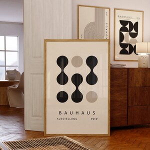 May include: A framed poster with a geometric design in black and beige. The poster has the text "BAUHAUS AUSSTELLUNG 1919" at the bottom.