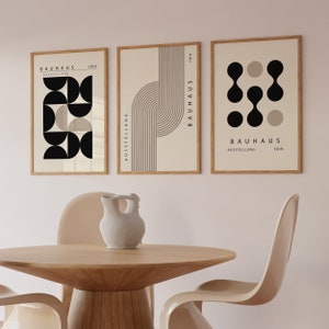 May include: Three framed prints with a minimalist design featuring black and beige geometric shapes and the text "BAUHAUS AUSSTELLUNG 1919".