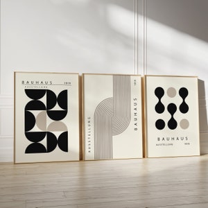 May include: Three minimalist art prints with geometric shapes in black and beige on a cream background. The prints feature the text "Bauhaus Ausstellung 1919".