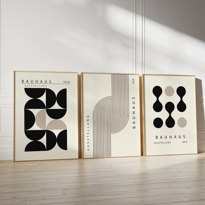 May include: Three minimalist art prints with geometric shapes in black and beige on a cream background. The prints feature the text "Bauhaus Ausstellung 1919".