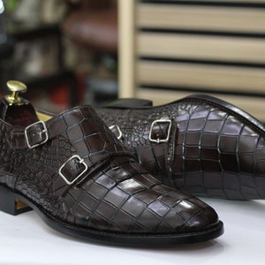 May include: A pair of brown leather double monk strap shoes with a crocodile embossed pattern.
