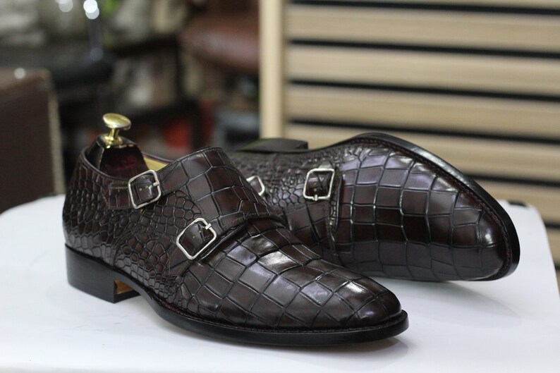 May include: A pair of brown leather double monk strap shoes with a crocodile embossed pattern.