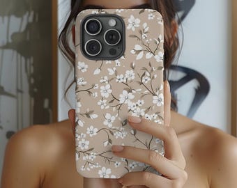 Könnte beinhalten: Eine beige Handyhülle mit einem weißen Blumenmuster. Die Hülle hat einen Ausschnitt für das Kameraobjektiv und einen erhöhten Rand an den Kanten.