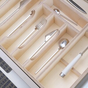 May include: A wooden cutlery organizer with various silverware pieces. The silverware includes knives, forks, and spoons, all with a shiny, metallic finish. The organizer is divided into compartments, each holding a different type of utensil.