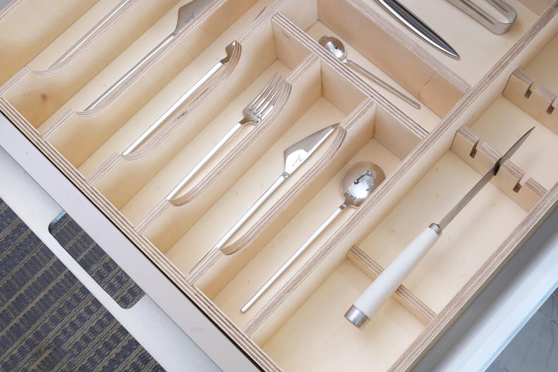 May include: A wooden cutlery organizer with various silverware pieces. The silverware includes knives, forks, and spoons, all with a shiny, metallic finish. The organizer is divided into compartments, each holding a different type of utensil.