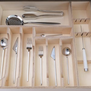 May include: A wooden drawer organizer filled with various stainless steel silverware. The set includes forks, knives, spoons, and serving utensils. The drawer is divided into compartments for organized storage of the cutlery.