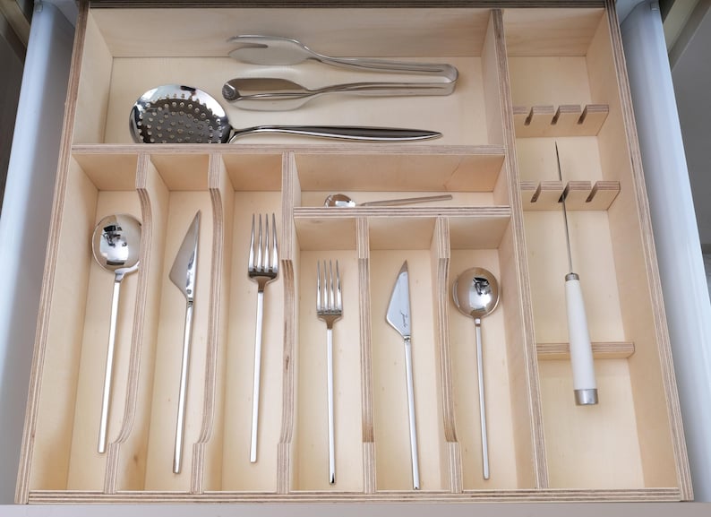 May include: A wooden drawer organizer filled with various stainless steel silverware. The set includes forks, knives, spoons, and serving utensils. The drawer is divided into compartments for organized storage of the cutlery.