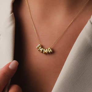 May include: A gold necklace with the name "EMMA" spelled out in individual gold letters.