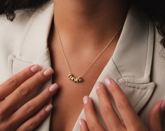 May include: A gold necklace with a name spelled out in individual letters. The letters are connected together and form a curved shape.