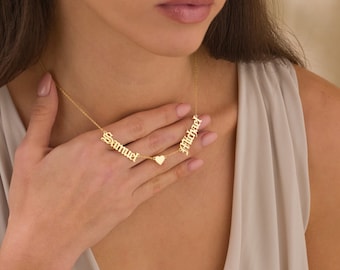 May include: Gold necklace with two names, "Samuel" and "Michael", in an old English font, connected by a small heart charm.