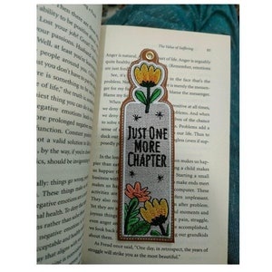 May include: A brown bookmark with colorful embroidered flowers and the text "Just One More Chapter".