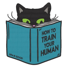 May include: A black cat with green eyes is reading a blue book that says "How to Train Your Human" on the cover. The book has the words "Life is Good" on the bottom left corner.