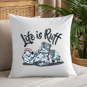 Könnte beinhalten: Weißes quadratisches Kissen mit einem gestickten Design mit zwei Dalmatiner-Welpen und dem Schriftzug "Life is Ruff" in schwarzer Schrift. Ein Welpe trägt eine rosa Schleife, der andere einen grauen Hut und ein rotes Halsband.