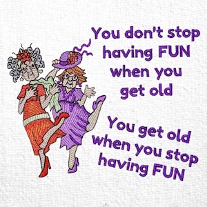 Może przedstawiać: Haftowany wzór na białej tkaninie przedstawiający dwie starsze kobiety tańczące. Jedna ma na sobie pomarańczową sukienkę, a druga fioletową. Tekst brzmi: "Nie przestajesz się bawić, gdy się starzejesz. Starzejesz się, gdy przestajesz się bawić."