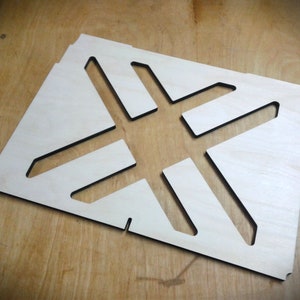 Può includere: Un ritaglio di legno con un design geometrico. Il ritaglio ha la forma di una stella a quattro punte ed è bordato di nero.