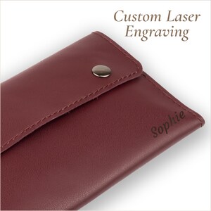 May include: A burgundy leather wallet with a silver snap closure. The text "Custom Laser Engraving" is above the wallet, and the name "Sophie" is engraved on the front.