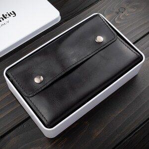 May include: A black leather wallet with a snap closure, presented in a white box. The wallet is rectangular and has a smooth texture. The box has the brand name "M&uuml;nkiy ITALY" printed on the lid.