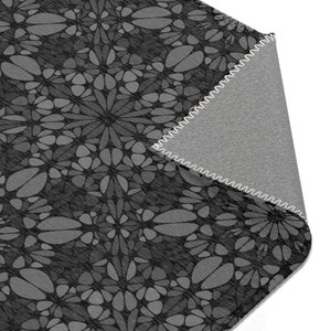 May include: A black and gray patterned rug with a fringed edge. The rug is made of a soft, textured fabric.