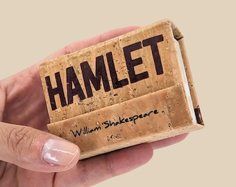 May include: A small, cork-covered book with the title "HAMLET" printed in black on the front. The author, "William Shakespeare", is printed in black on the bottom of the front cover.
