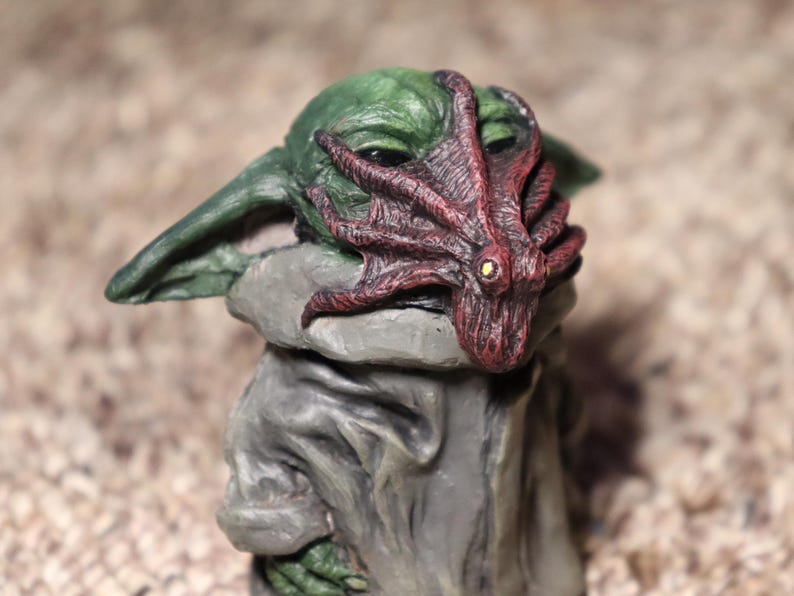 May include: A green and gray figurine of a character wearing a red and brown octopus mask.