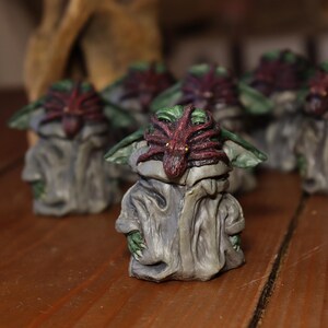 May include: A group of small, hand-painted figurines of a fictional character. Each figurine is painted in shades of green, brown, and red. The character has a large head with large eyes and a small mouth. The character is wearing a grey robe with a red and green spider-like creature on its head.