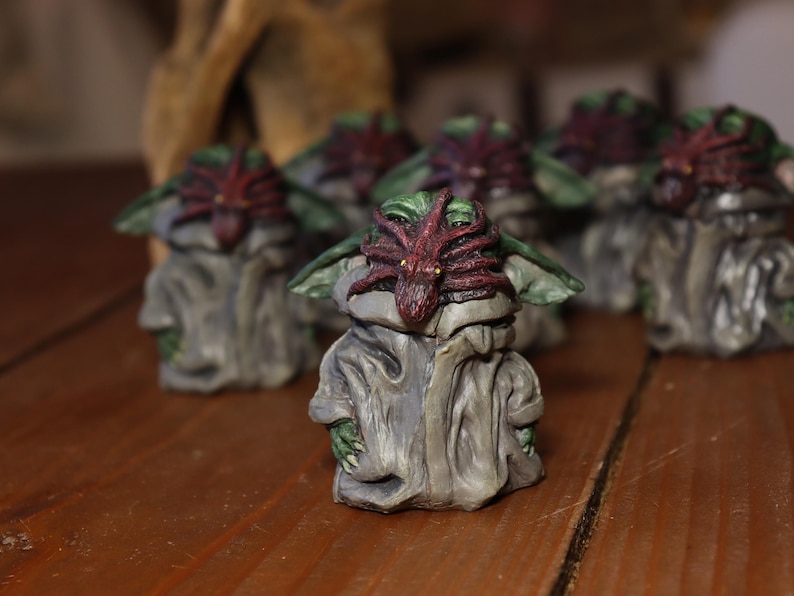 May include: A group of small, hand-painted figurines of a fictional character. Each figurine is painted in shades of green, brown, and red. The character has a large head with large eyes and a small mouth. The character is wearing a grey robe with a red and green spider-like creature on its head.