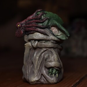 May include: A small, green and red figurine with a detailed, textured surface. The figurine has a large, tentacled head and a hooded robe.