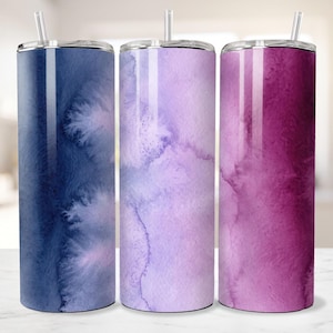 May include: Three cylindrical tumblers with lids and clear straws. The left tumbler features a deep navy blue watercolor wash, the center is a light lavender watercolor, and the right tumbler displays a vibrant magenta watercolor pattern.