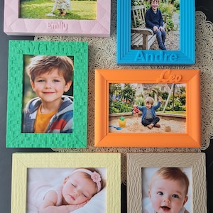 Könnte beinhalten: Eine Sammlung von sechs farbigen Bilderrahmen, die jeweils ein Foto enthalten. Die Rahmen sind in verschiedenen Farben erhältlich, darunter Rosa, Blau, Grün, Orange, Gelb und Beige. Jeder Rahmen hat eine strukturierte Oberfläche und einen Namen.