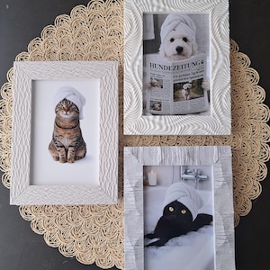 Könnte beinhalten: Drei gerahmte Drucke mit Tieren in Spa-Szenen. Eine getigerte Katze mit Handtuch, ein Hund liest Zeitung und eine schwarze Katze in der Badewanne. Die weißen Rahmen haben eine strukturierte Oberfläche. Die Zeitung ist auf Deutsch.