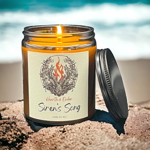 May include: A brown glass candle jar with a black lid. The label reads "Hearth & Ember Siren's Song 100% Soy Wax". The candle is lit and the flame is visible.