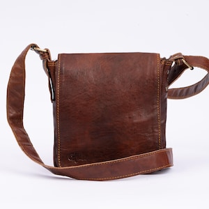 Könnte beinhalten: Eine braune Leder-Umhängetasche mit einem langen, verstellbaren Trageriemen. Die Tasche hat einen Klappverschluss und ein kleines Fach auf der Vorderseite.