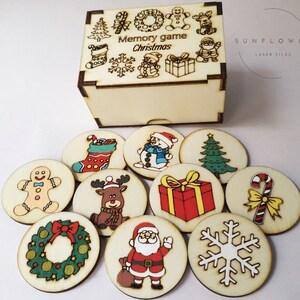 May include: A wooden Christmas memory game. The box and circular game pieces are made of light-colored wood. The box is engraved with festive images and the words "Memory game Christmas". The game pieces feature colorful holiday illustrations.